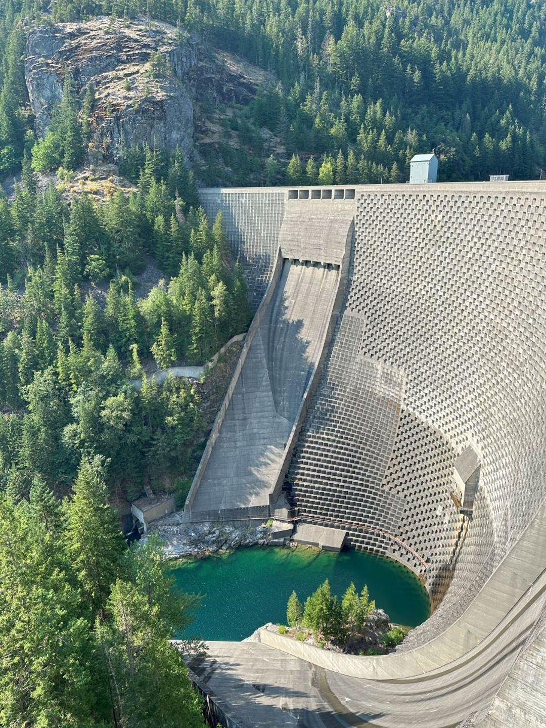 A large dam with a unique architectural design surrounded by trees and water
