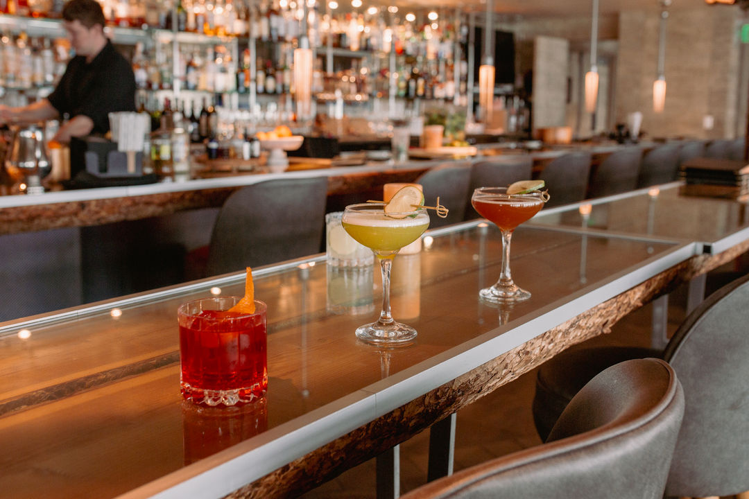 A bar with three cocktails on the counter and a bartender in the background