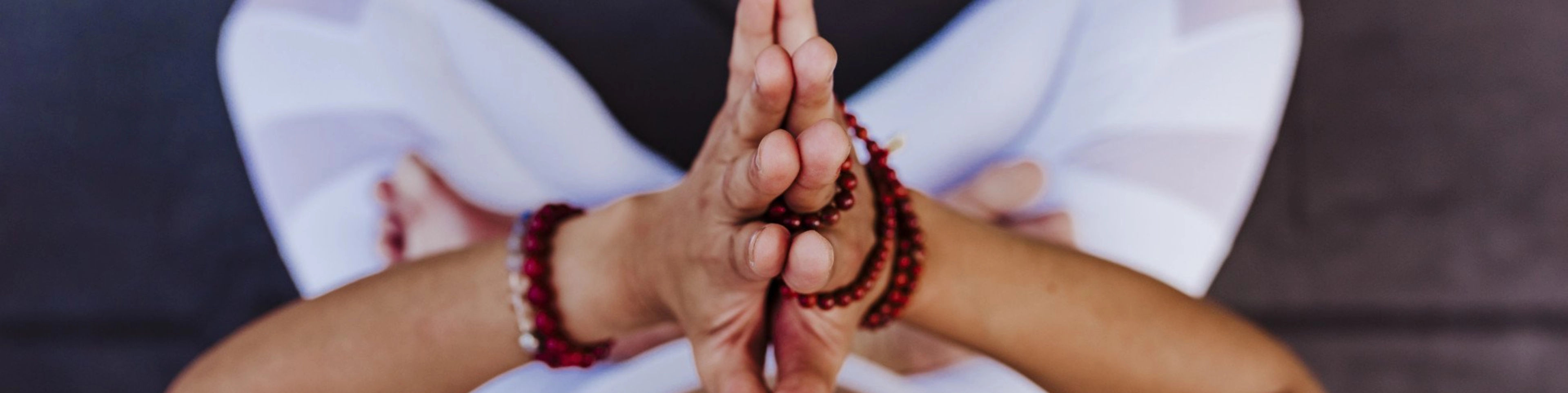 Person in a seated meditation pose with hands in prayer position and wearing a beaded bracelet