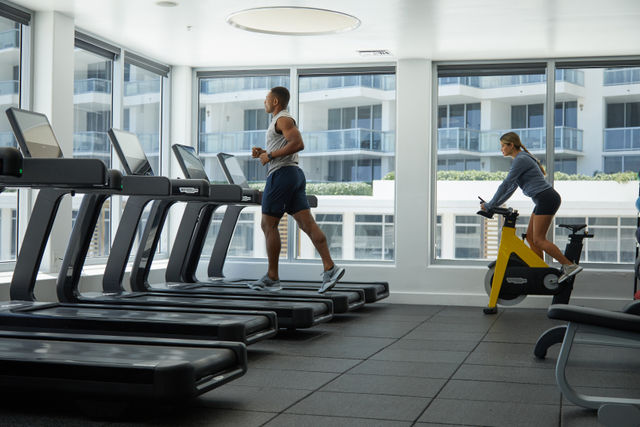 A man and woman exercising in a modern gym with treadmills and an exercise bike.