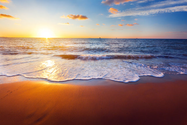 A serene beach scene at sunset with waves gently lapping at the shore.
