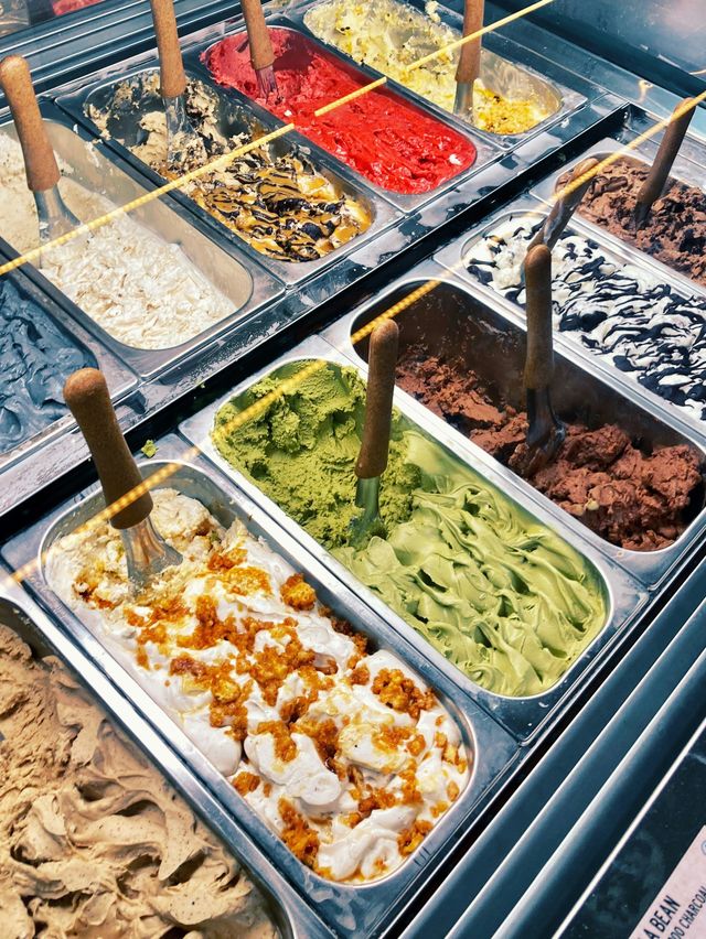A display of various ice cream flavors in metal containers.