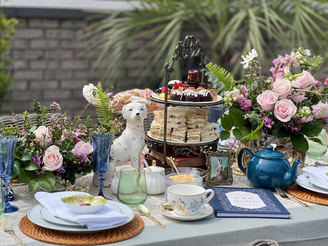 A table set for tea with a cake stand, flowers, and a dog statue