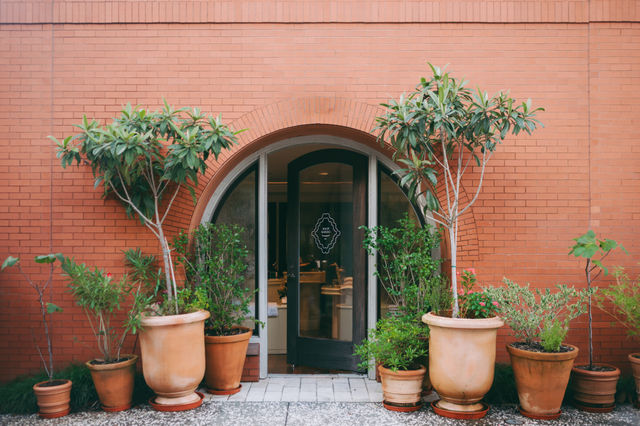 A red brick building with an arched doorway and potted plants outside.
